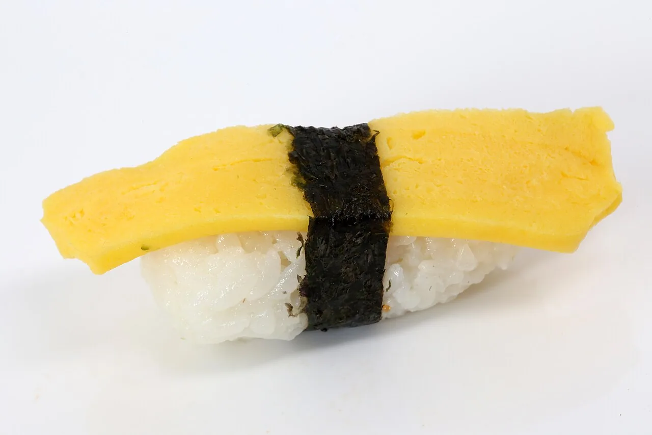 Tamago nigiri sushi with a folded omelette topping and a strip of nori